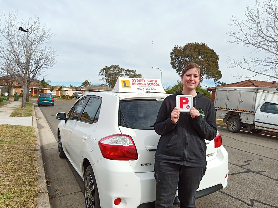 Amanda holding red P plates beside the Sydney South Driving School car after passing her driving test