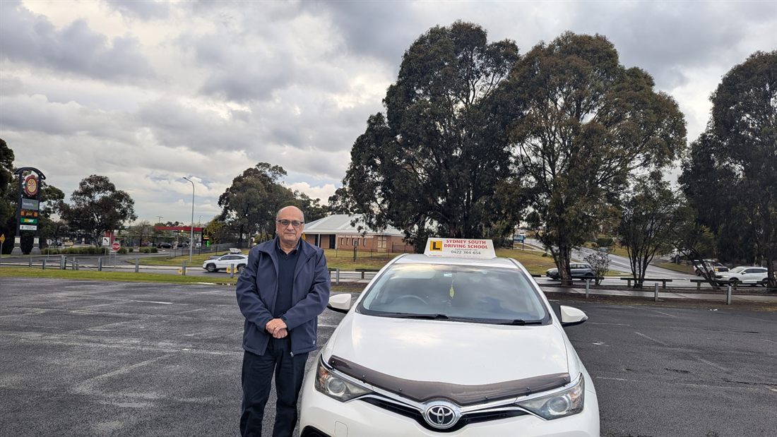 Ashraf George, senior driving instructor at Sydney South Driving School, beside a dual-control automatic car in Liverpool NSW
