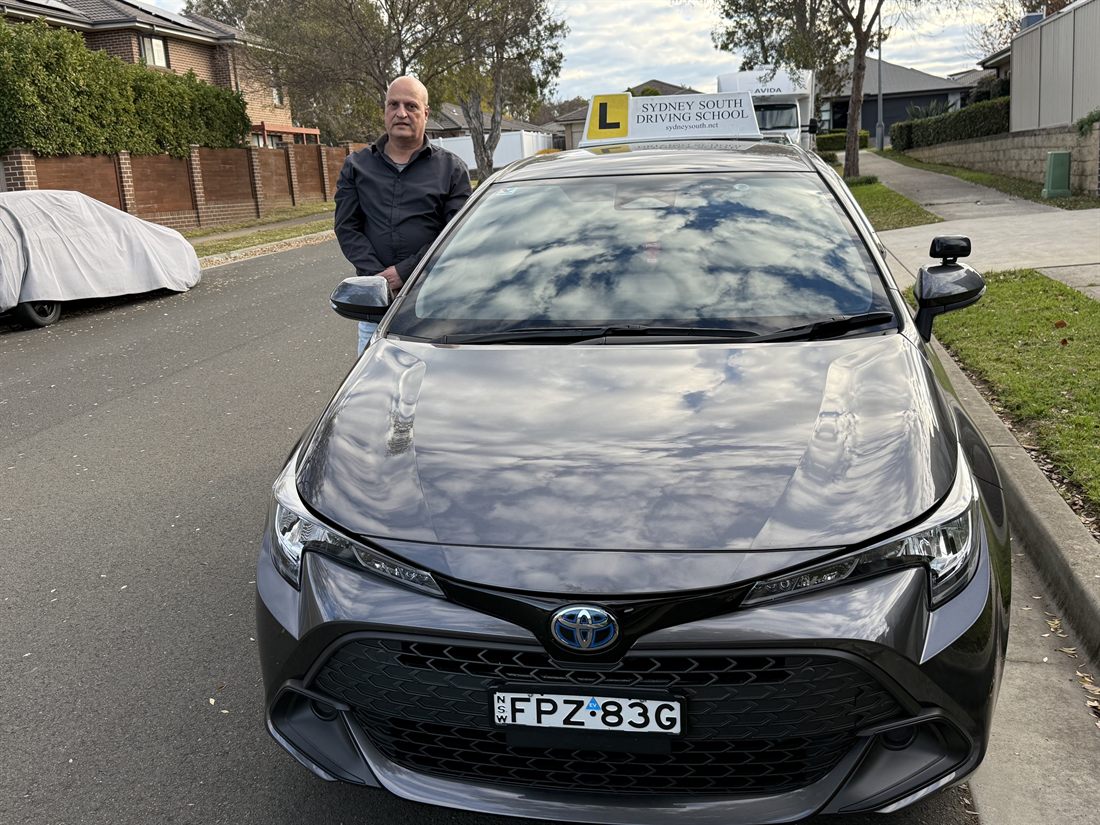 George, senior driving instructor at Sydney South Driving School, standing beside the Sydney South driving school Corolla