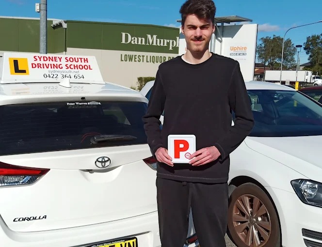Student holding red P plates beside the Sydney South Driving School car