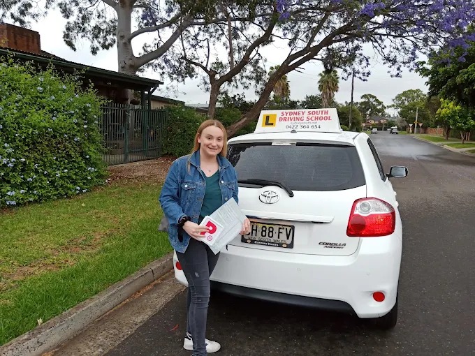 Student holding red P plates beside the Sydney South Driving School car on a local street
