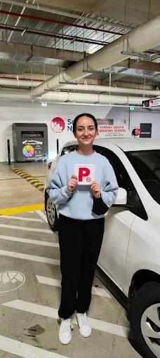 Student holding red P plates beside a white car after passing the driving test