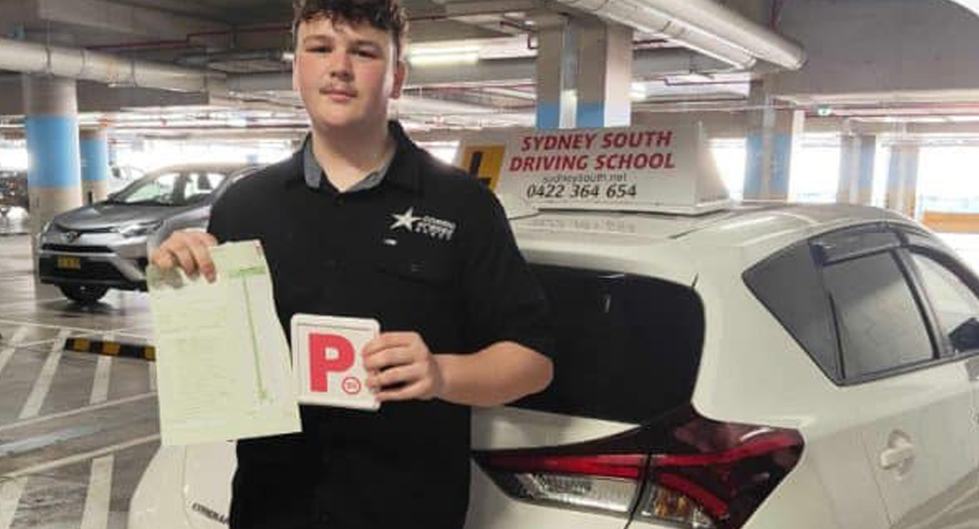 Student holding red P plates and a pass certificate beside the Sydney South Driving School car